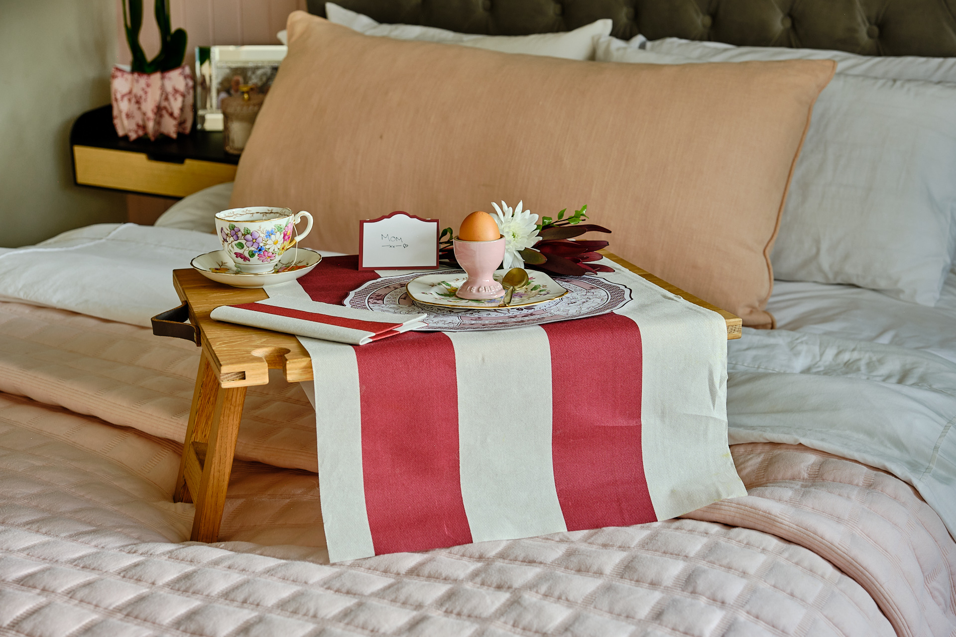 Elegant Mother’s Day breakfast in bed tray with tea, soft-boiled egg, flowers, and a wine striped table runner.